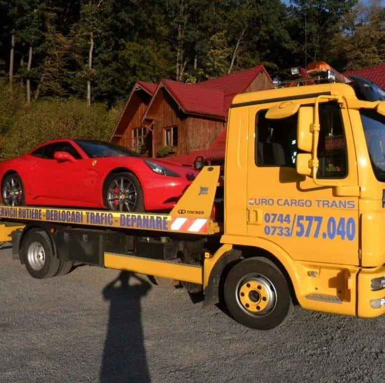 Ferrari roșu încărcat pe platforma noastră MAN, în fața unui showroom