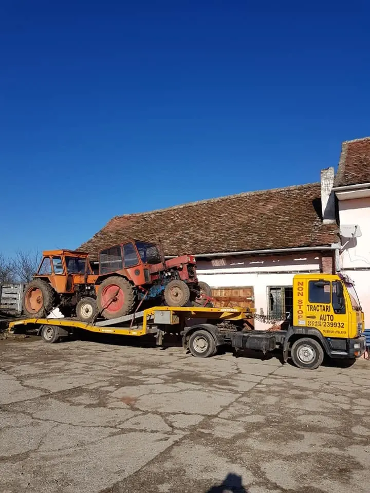 Tractor roșu transportat pe platforma MAN